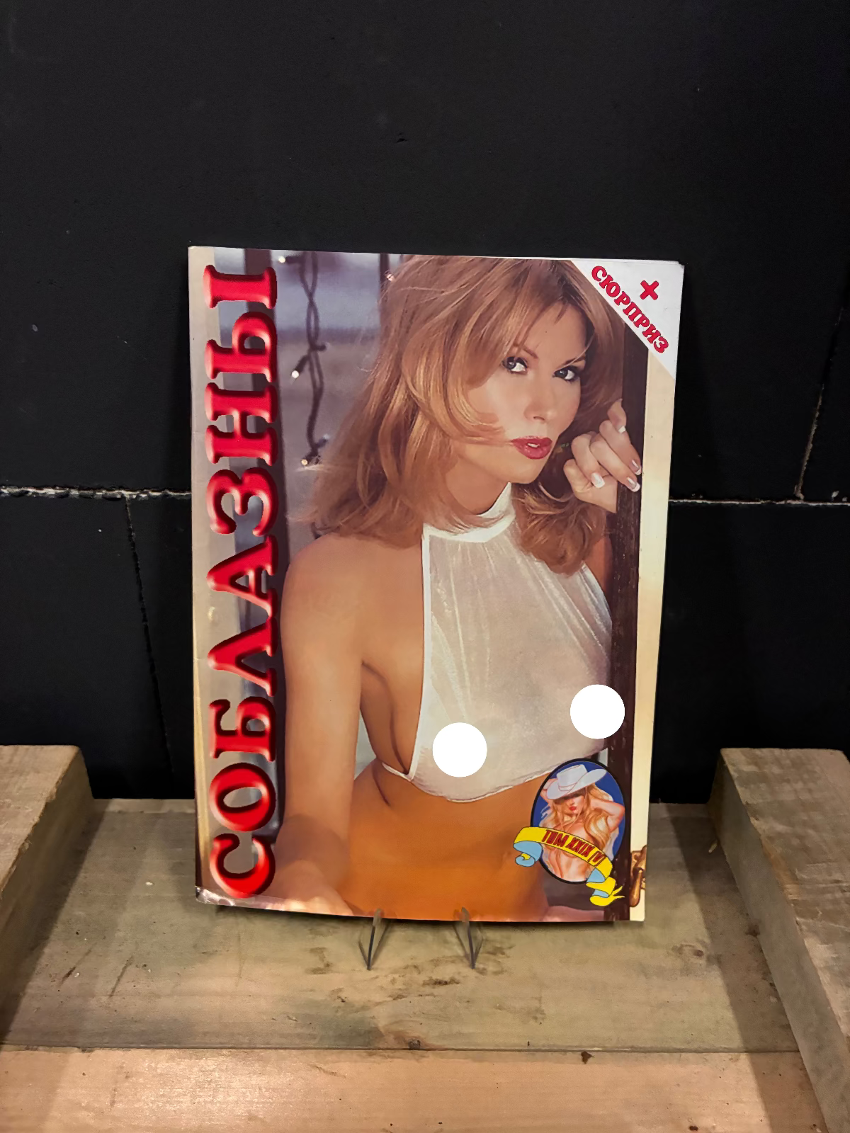A physical copy of a Russian Orthodox church bulletin or booklet titled 'СОБЛАЗНЫ' (Soblazy) featuring a blonde woman in a white top, displayed on a wooden stand against a dark background.