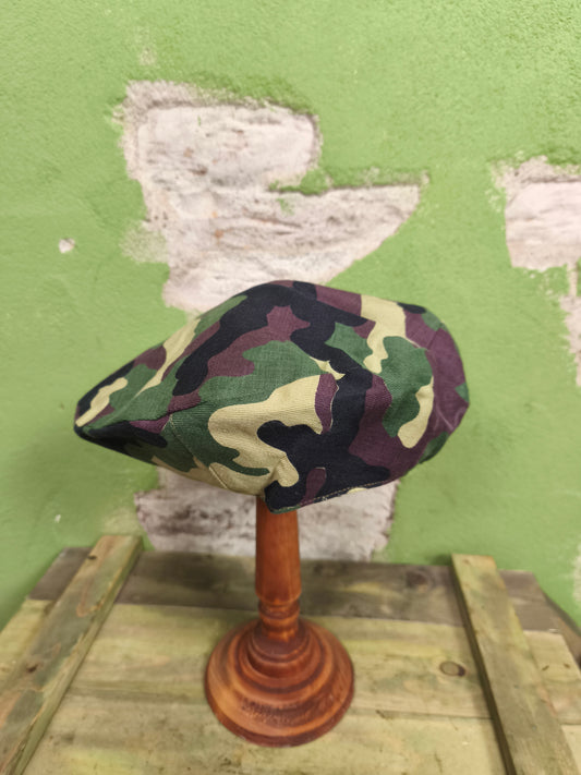 Camouflage-patterned hat on a wooden stand against a green wall with peeling paint.
